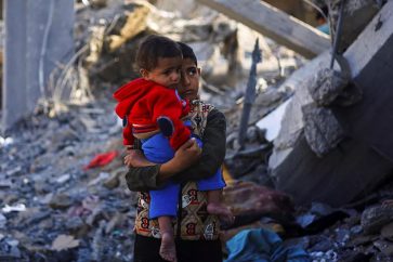 Un garçon palestinien portant un bébé se tient près d’une maison détruite par une frappe israélienne, à Rafah, dans le sud de la bande de Gaza. ©Reuters